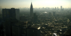 A dense high-rise city skyline obscured by heavy gray smog and haze, conveying a polluted dystopian urban atmosphere