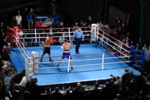 An empty, brightly lit professional boxing ring viewed from outside the ropes