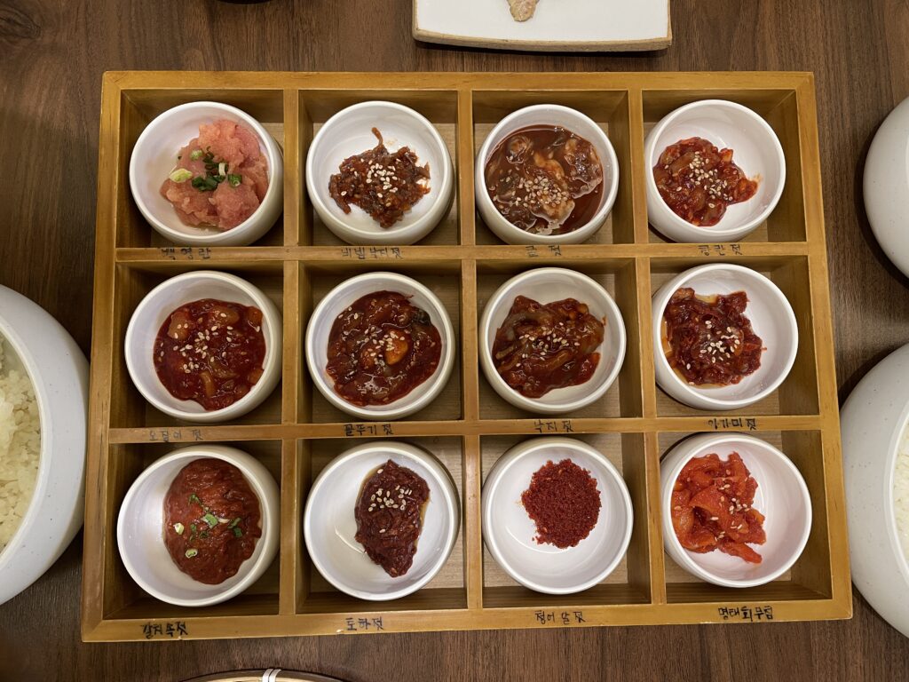 젓갈 (Jeotgal) — Korean fermented/salted-seafood, the core of a 젓갈백반 (jeotgal-baekban) banchan set — a representative photo of the dish, not necessarily from the restaurants above. Photo: Photo by Jo Hanshin (own work), via Wikimedia Commons "File:Jeotgal (Salted Seafood), Koean Food.jpg". License: CC0 1.0 (no attribution legally required).