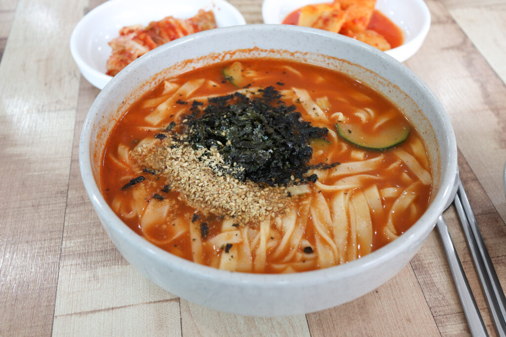 장칼국수 (jang-kalguksu) — Korean noodle soup in a gochujang/doenjang-based spicy paste broth — a representative photo of the dish, not necessarily from the restaurants above. Photo: Mobius6, own work, via Wikimedia Commons, CC BY-SA 4.0