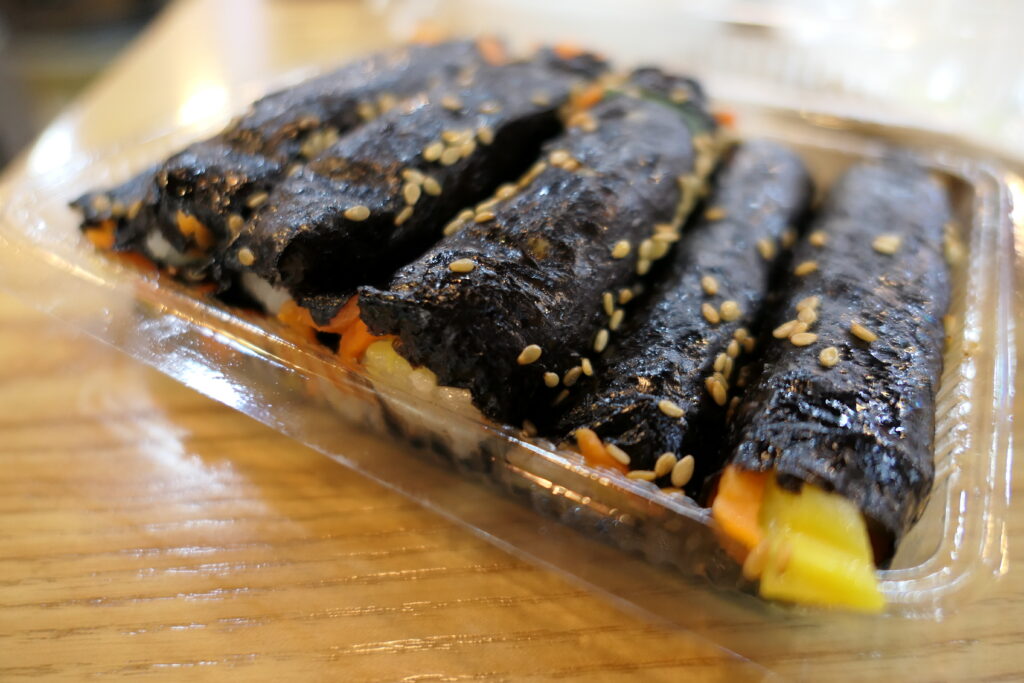 마약김밥 (Mayak-gimbap / mini gimbap) — a representative photo of the dish, not necessarily from the restaurants above. Photo: Photo by bryan (bryan... from Taipei, Taiwan), via Wikimedia Commons, licensed CC BY-SA 2.0 (https://creativecommons.org/licenses/by-sa/2.0). File: Mayak-gimbap (31896881761).jpg