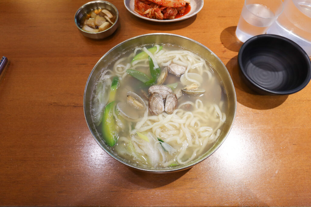 바지락칼국수 (Bajirak-kalguksu / clam knife-noodle soup) — a representative photo of the dish, not necessarily from the restaurants above. Photo: Photo by Mobius6 (own work), via Wikimedia Commons. Licensed under CC BY-SA 4.0 (https://creativecommons.org/licenses/by-sa/4.0). Source: https://commons.wikimedia.org/wiki/File:Bajirak-kalguksu_20230126_001.jpg