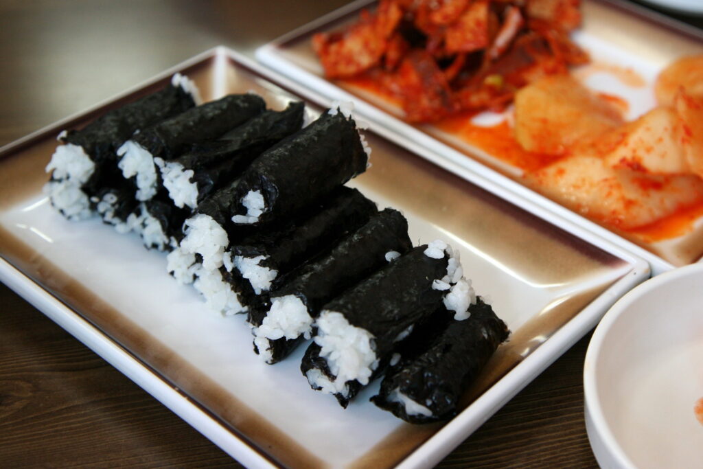 충무김밥 (Chungmu gimbap) — a representative photo of the dish, not necessarily from the restaurants above. Photo: Junho Jung (via Flickr, from South Korea); licensed CC BY 3.0 (https://creativecommons.org/licenses/by/3.0). VRT permission confirmed (ticket #2009092210040338). Source: https://commons.wikimedia.org/wiki/File:Korea-Tongyeong_food-Chungmu_gimbap-01.jpg