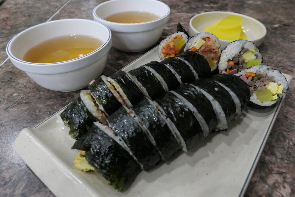 Gimbap served with danmuji (yellow pickled radish) on the side, a classic pairing. Photo: bryan..., via Wikimedia Commons.