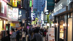 A crowded Seoul street at night glowing with dense neon Korean shop signs