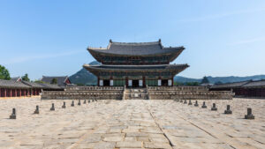 Front view of the wooden Geunjeongjeon throne hall and stone courtyard at Gyeongbokgung Palace under a blue sky