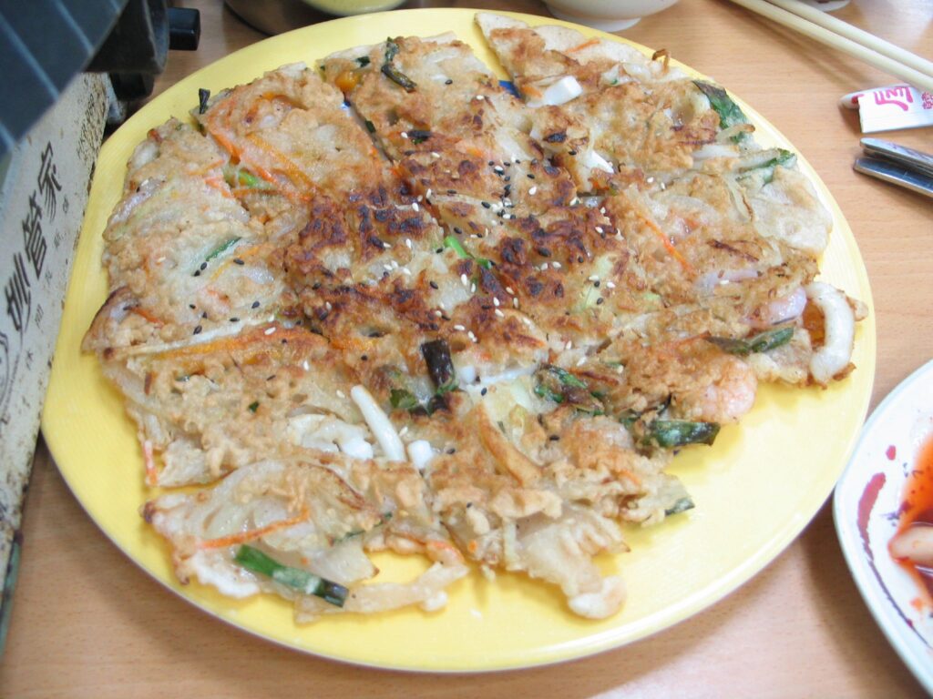 Haemul-pajeon cooking, scallions laid side by side and studded with seafood.