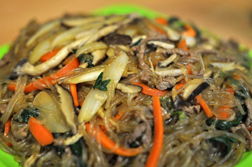 A plated serving of japchae, finished with toasted sesame seeds and a drizzle of sesame oil (참기름).