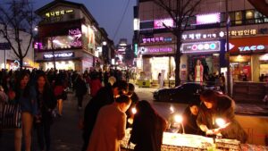 Neon signs and illuminated storefronts line a busy night street in Seoul's Hongdae entertainment district