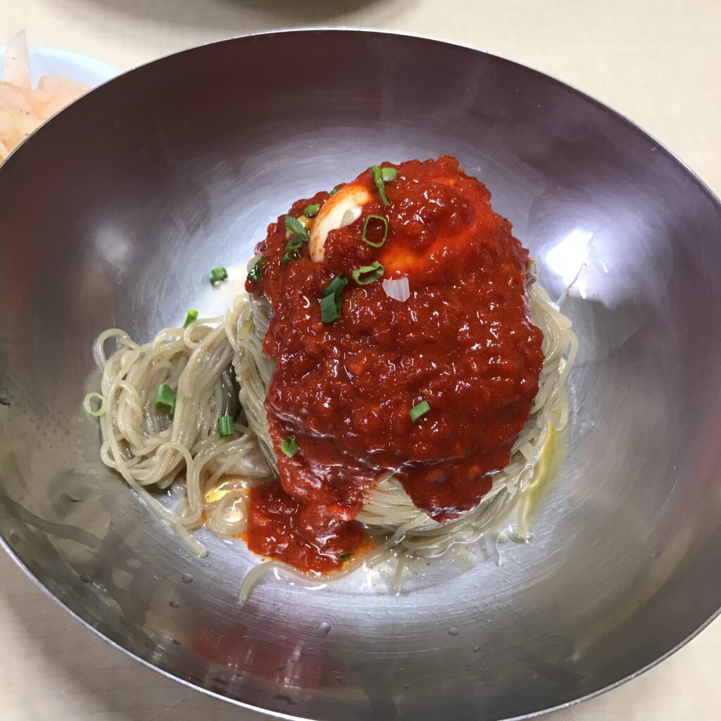 Bibim-naengmyeon: the same chewy noodles tossed hard in a sweet-spicy gochugaru sauce, no broth. (Photo: chomjong, CC BY 2.0, via Wikimedia Commons)