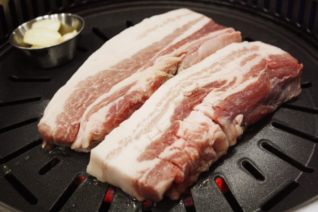 Pork belly (samgyeopsal) close-up on the grill, showing the alternating layers of lean and fat. (Photo: idkjm123 via Pixabay, CC0 / public domain)