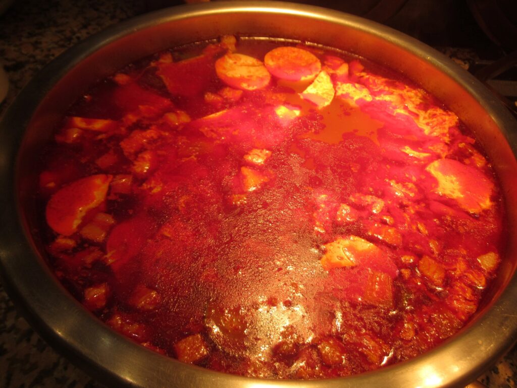 A close-up of the finished stew: silky soft tofu in red chili-oil broth with a raw egg cracked in the center.